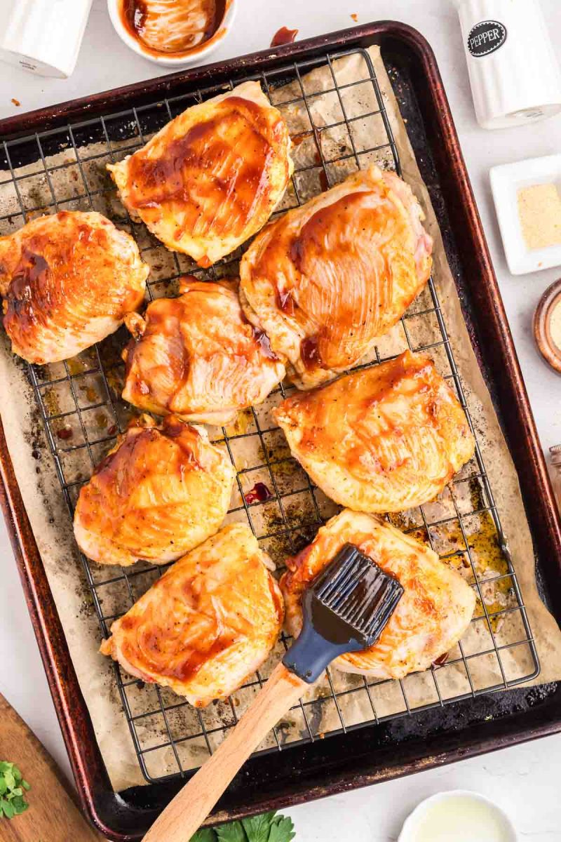 Barbecue sauce brushed onto baked chicken thighs on a wire rack ready for broiling. Hostess At Heart