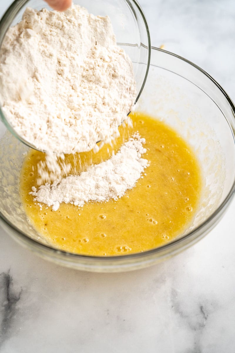 Mixed dry ingredients being added to the wet ingredients to make easy banana blueberry muffins. Hostess At Heart