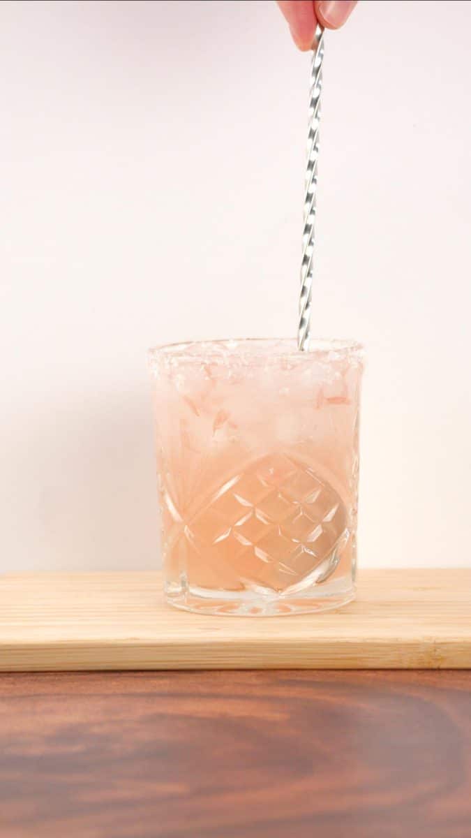 A mixing spoon stirring a Paloma drink in an ice filled low ball glass. Hostess At Heart