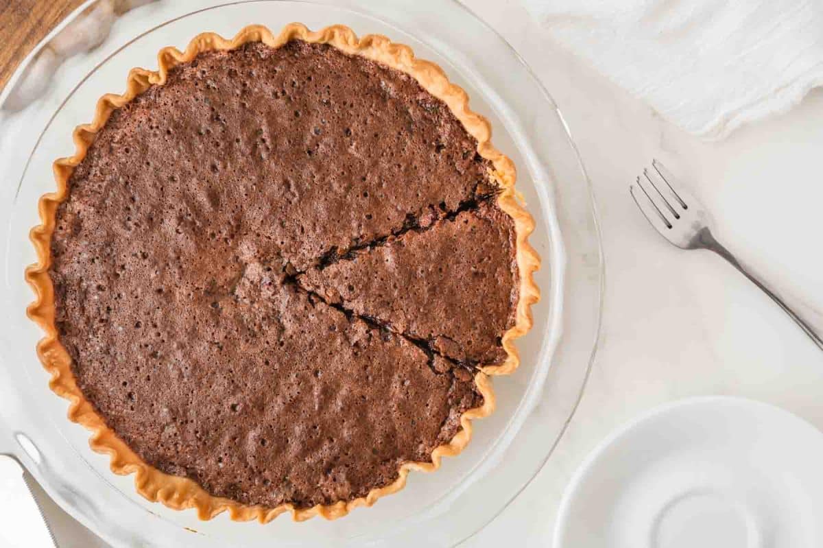 Top down view of an easy fudge pie baked in a golden brown pie crust with a flaky chocolate brownie top. Hostess At Heart