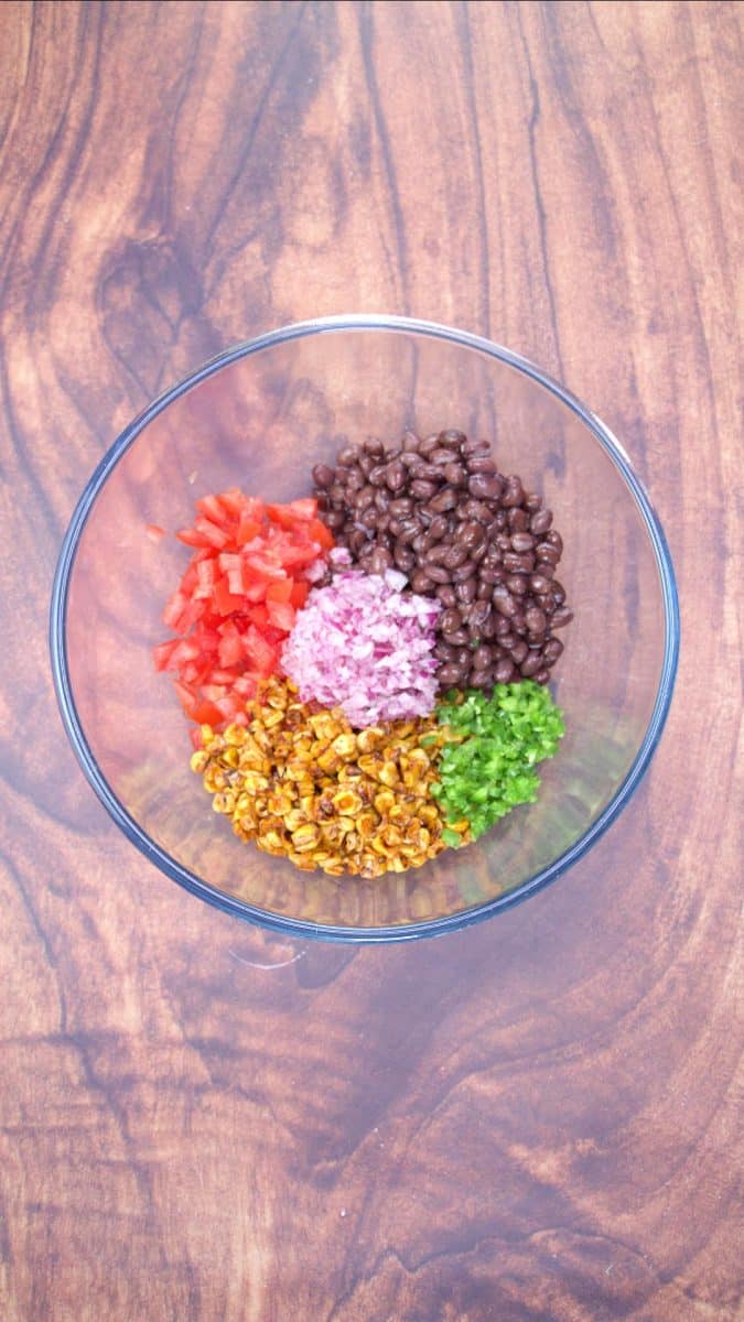 A mixing bowl filled with corn, black beans, jalapeno, tomatoes and red onion to make avocado salsa with corn and black beans - Hostess At Heart