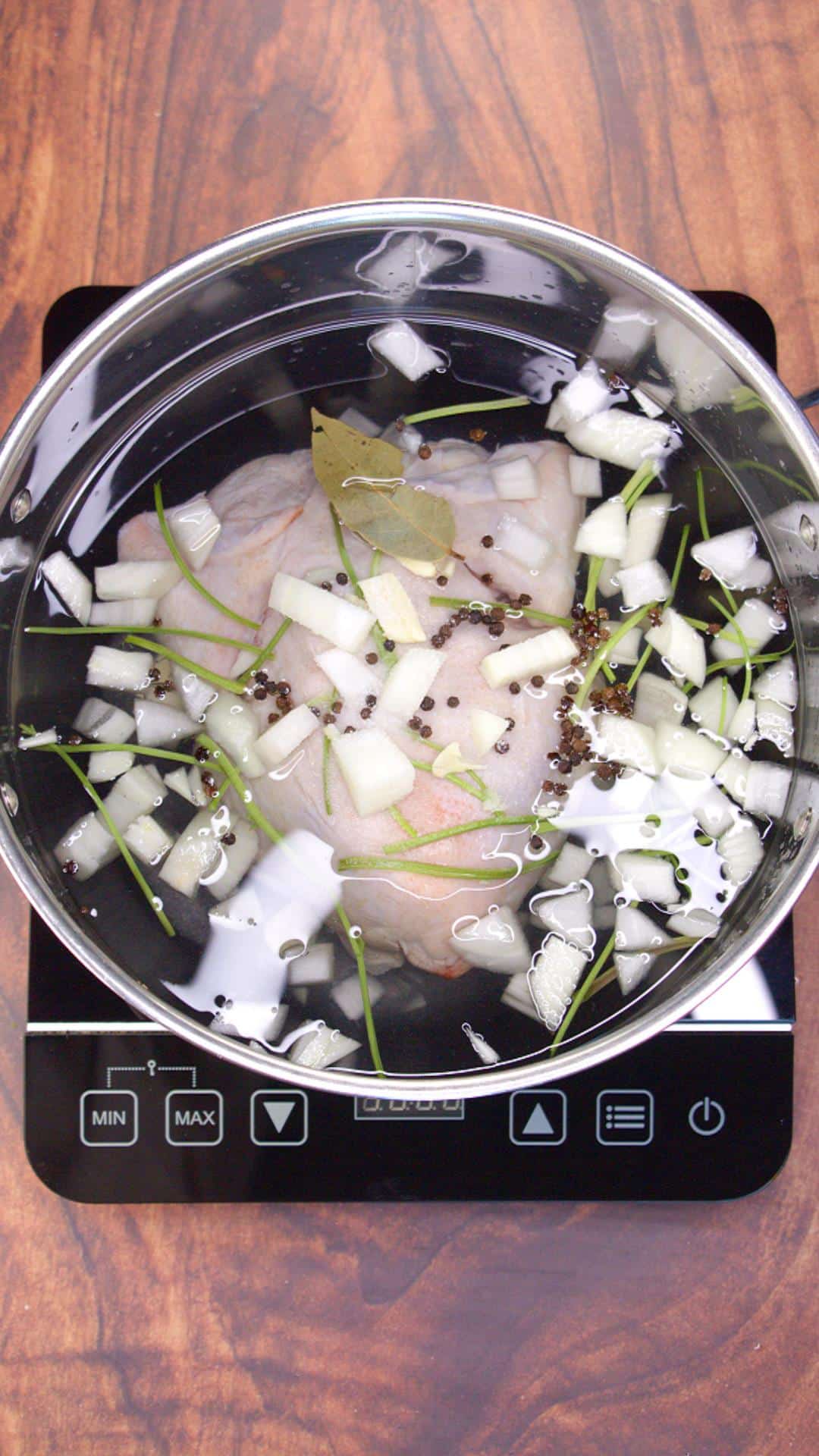 Whole chicken simmering in seasoned broth with cilantro, onion, garlic, and peppercorns in a Dutch oven. Hostess At Heart