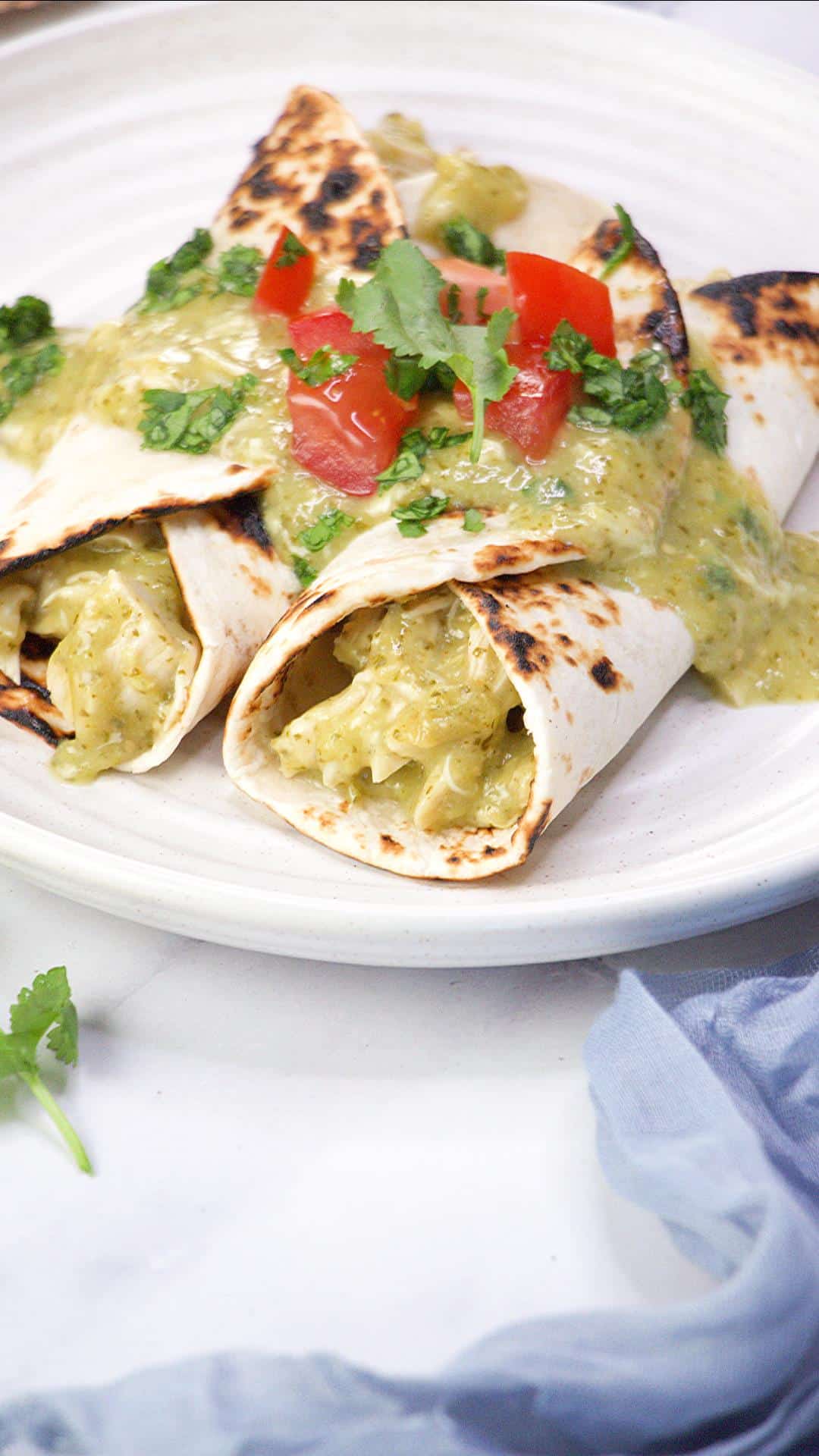 Table view of Two Green mole chicken enchiladas smothered in tomatillo sauce garnished with fresh tomatoes and cilantro. Hostess At Heart