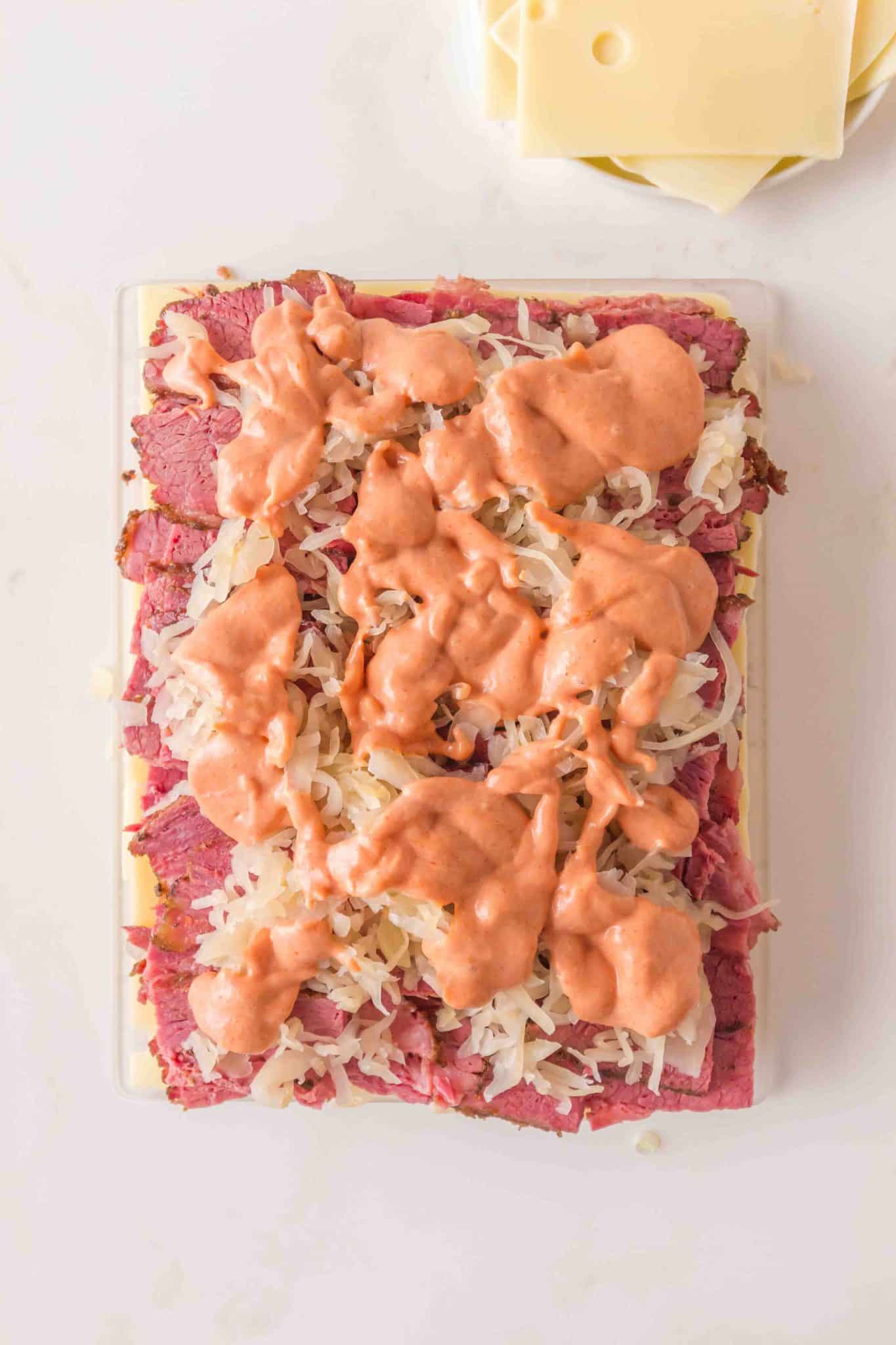 Drizzling homemade Thousand Island dressing over sauerkraut on corned beef sliders. Hostess At Heart