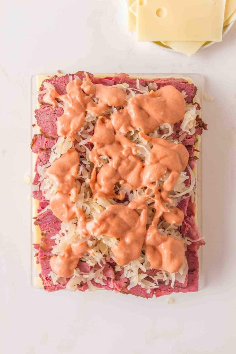 Drizzling homemade Thousand Island dressing over sauerkraut on corned beef sliders. Hostess At Heart