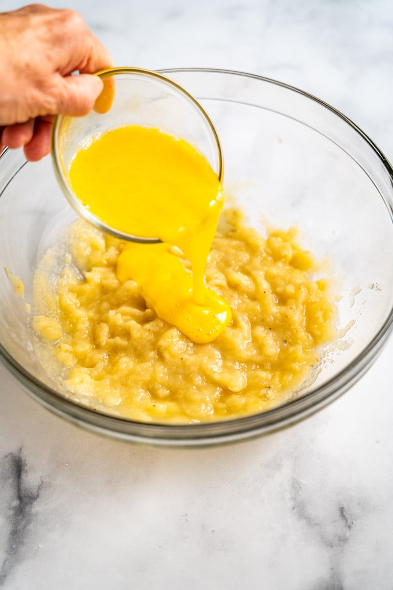 Beaten eggs added to a banana mixture in a mixing bowl to make moist banana blue berry muffins recipe. Hostess At Heart