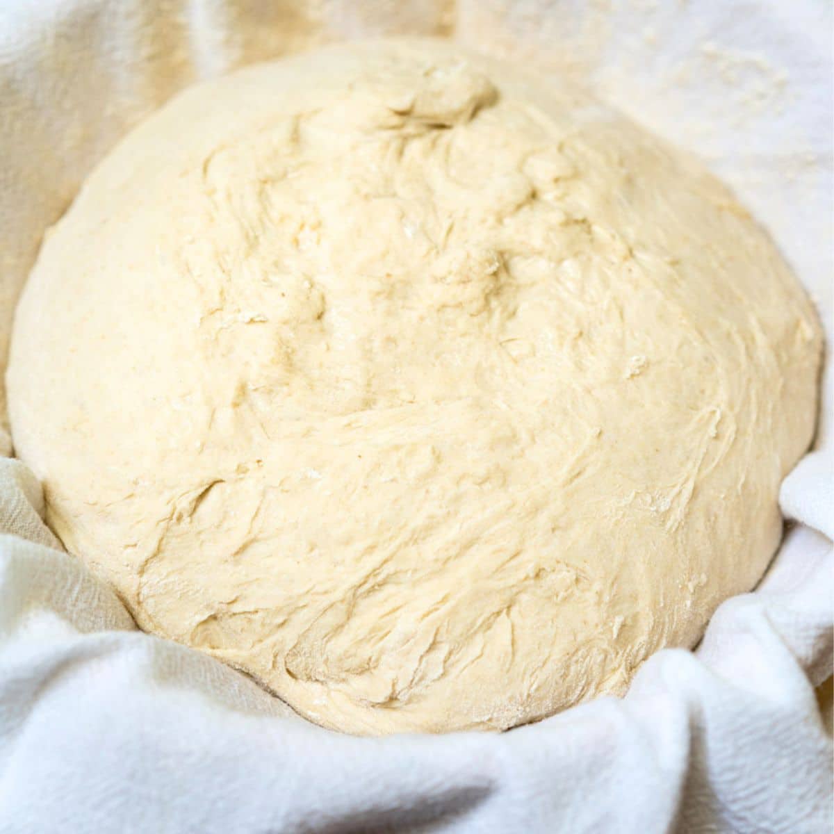 A flour sack towel covering a basket and filled with spelt sourdough bread dough ready for rising. Hostess At Heart