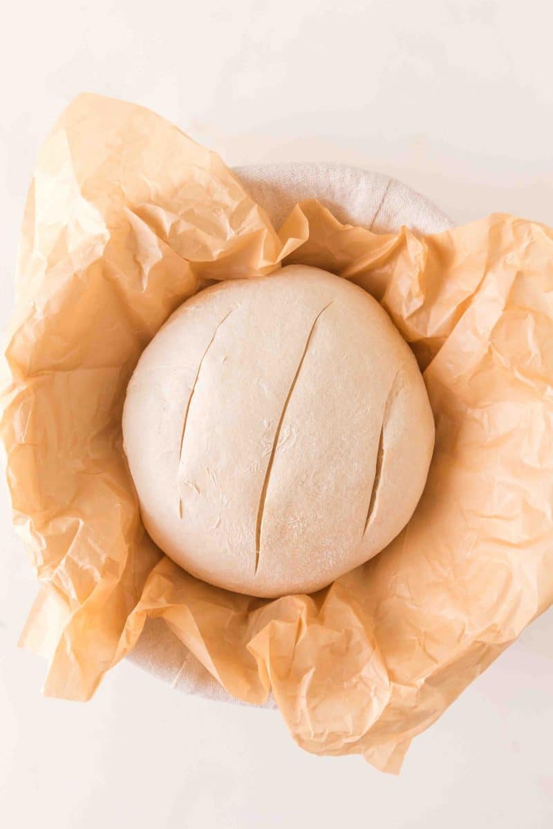 A round boule of overnight sourdough bread dough that's been scored 3 times and is ready to be baked. Hostess At Heart