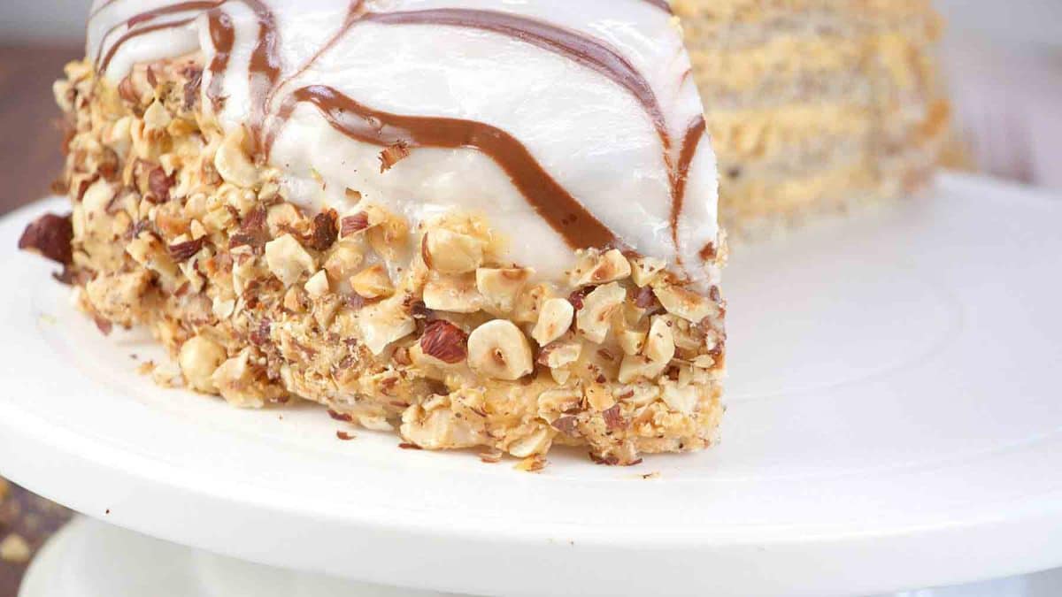 Whole Esterhazy Torte on a cake plate showing spiderweb chocolate design and hazelnut-crusted sides. Hostess At Heart