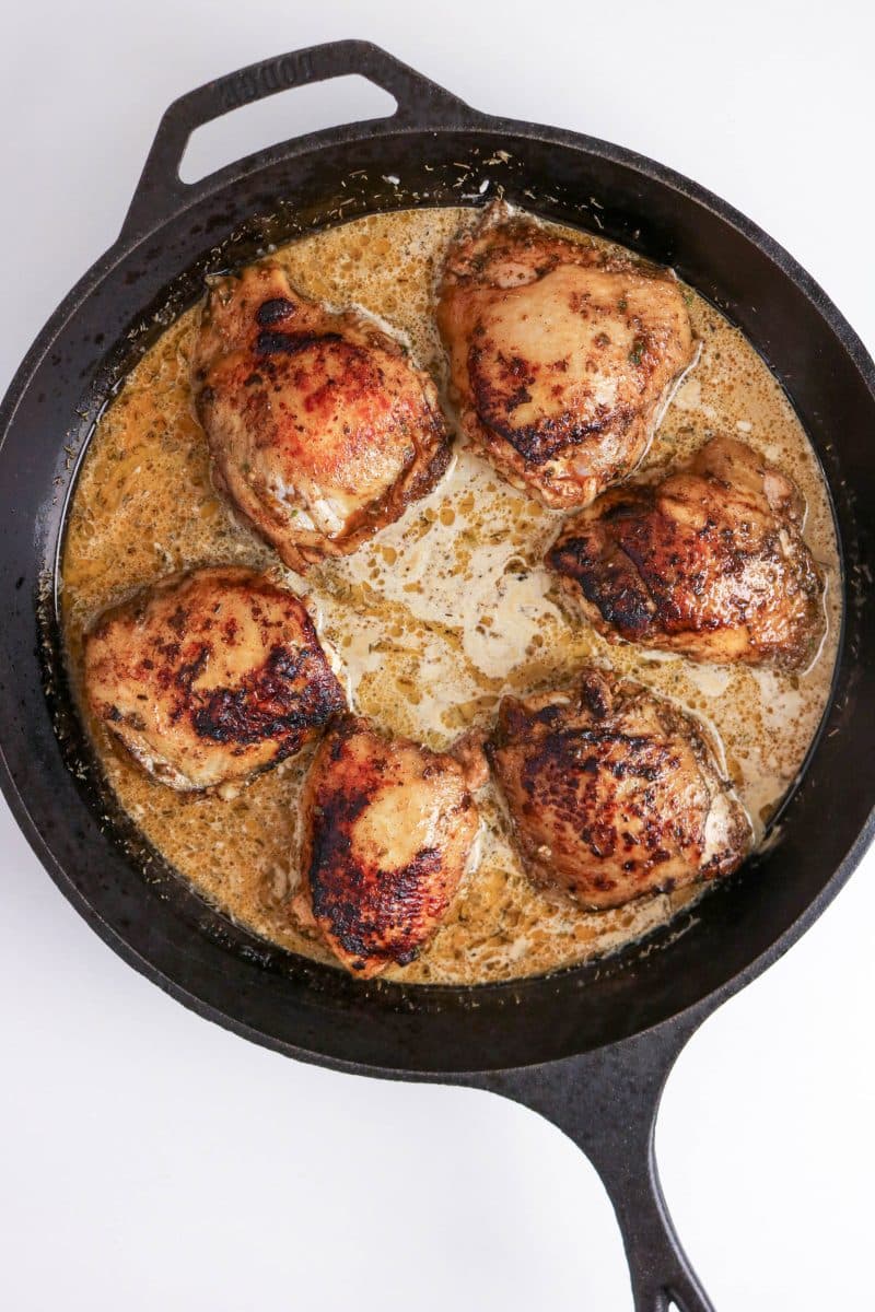 Seared jerk chicken thighs nestled skin-side up into coconut milk rice in a skillet ready for baking. Hostess At Heart