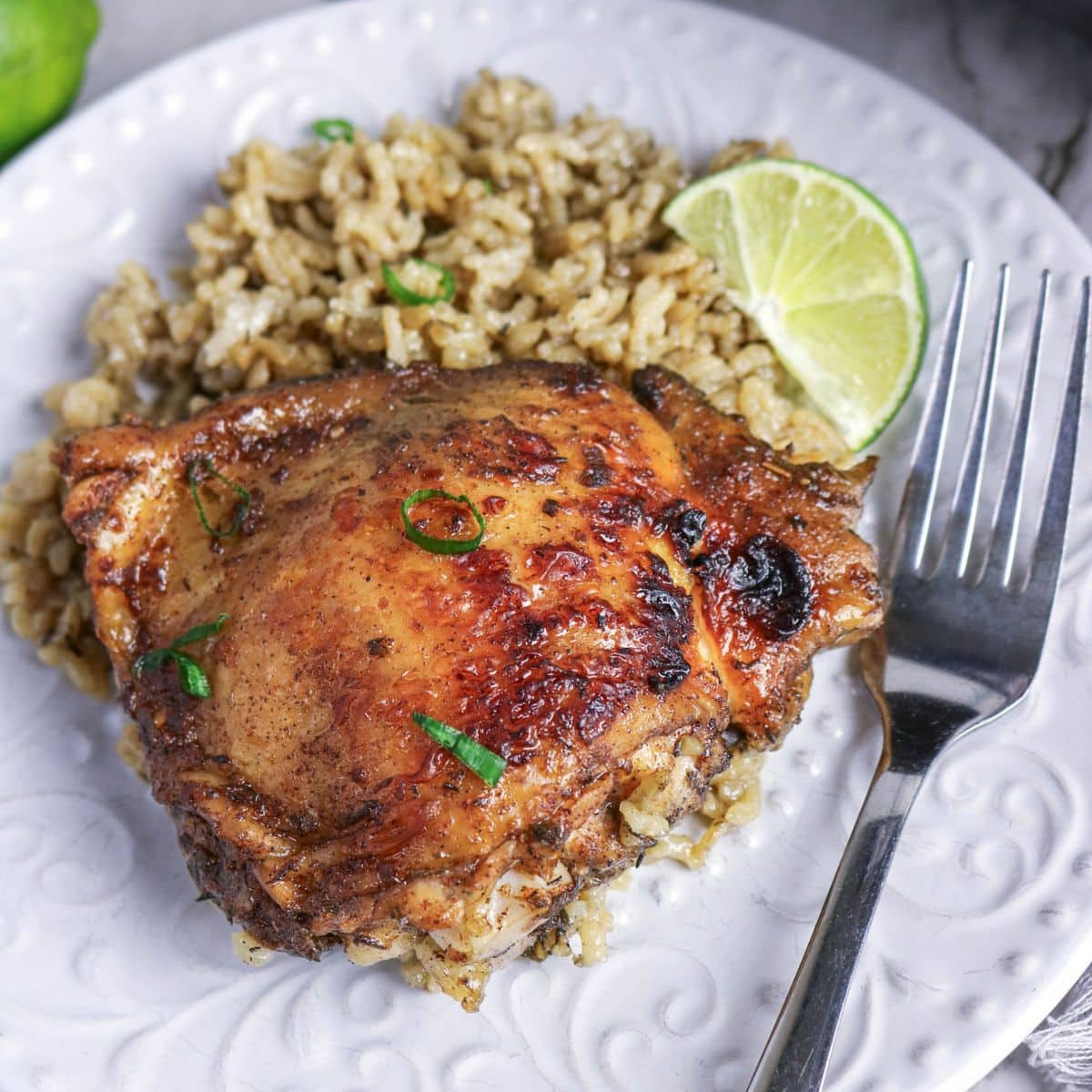 Top down view of a plated easy jerk chicken and rice plated on a white dish with fresh lime wedge. Hostess At Heart