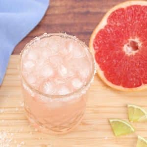 Quarter view of an easy Paloma cocktail in a salt rimmed lowball glass filled with ice. Hostess At Heart