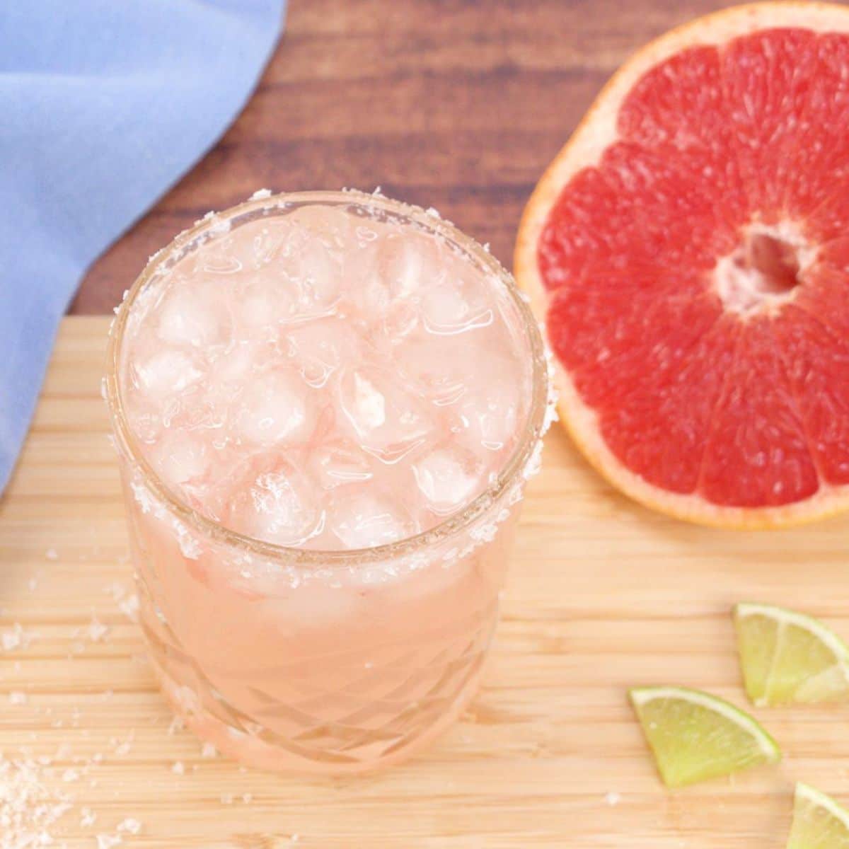 Quarter view of an easy Paloma cocktail in a salt rimmed lowball glass filled with ice. Hostess At Heart