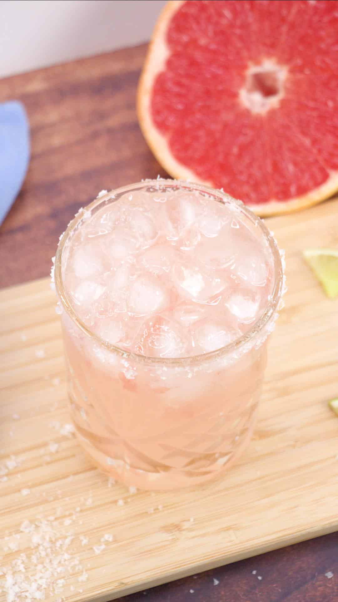 Quarter view of an easy Paloma grapefruit cocktail in a salt rimmed lowball glass filled with ice. Hostess At Heart