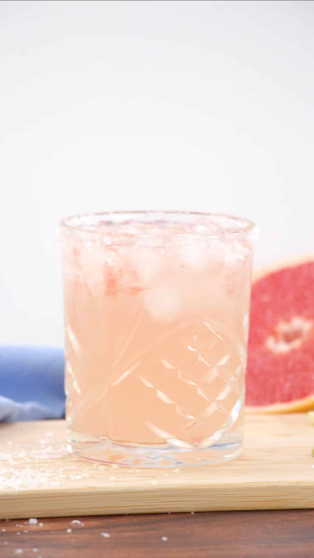 Closeup sideview of a chilled Paloma cocktail in an ice-filled rocks glass. Hostess At Heart