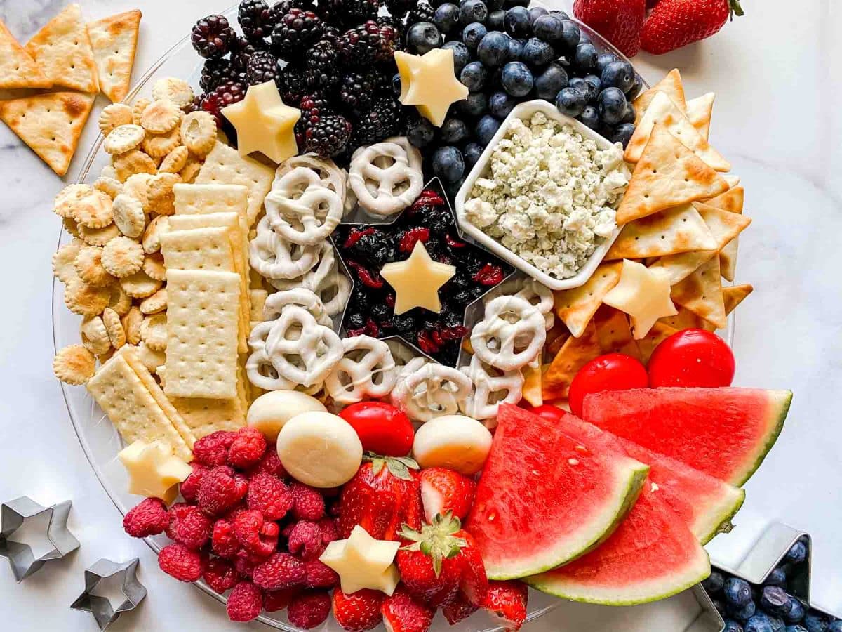 A party appetizer red white and blue grazing board filled with fruits, cheeses, crackers, and pretzels perfect for summer parties and holidays. Hostess At Heart