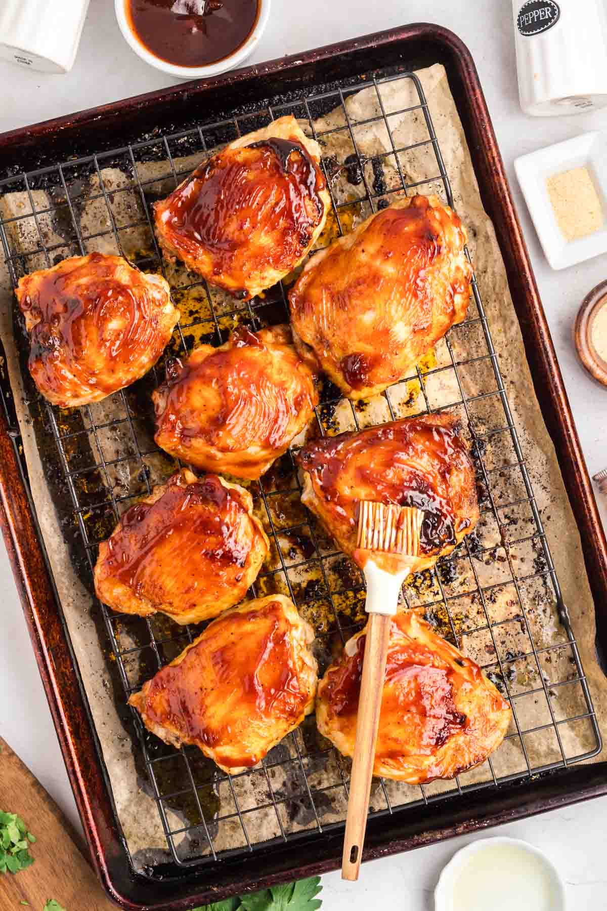 Baked BBQ chicken thighs on a rack sauced with thick barbecue sauce ready to be broiled. Hostess At Heart