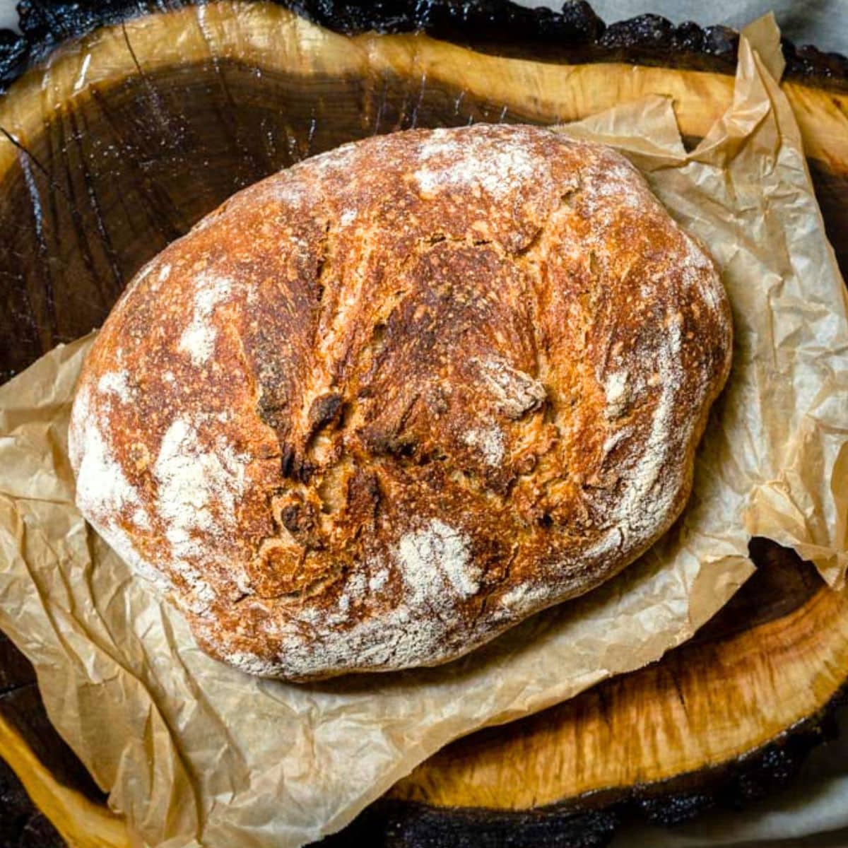 Angled view of a rustic boule of spelt sourdough bread brushed with patches of flour and baked to a golden brown. Hostess At Heart