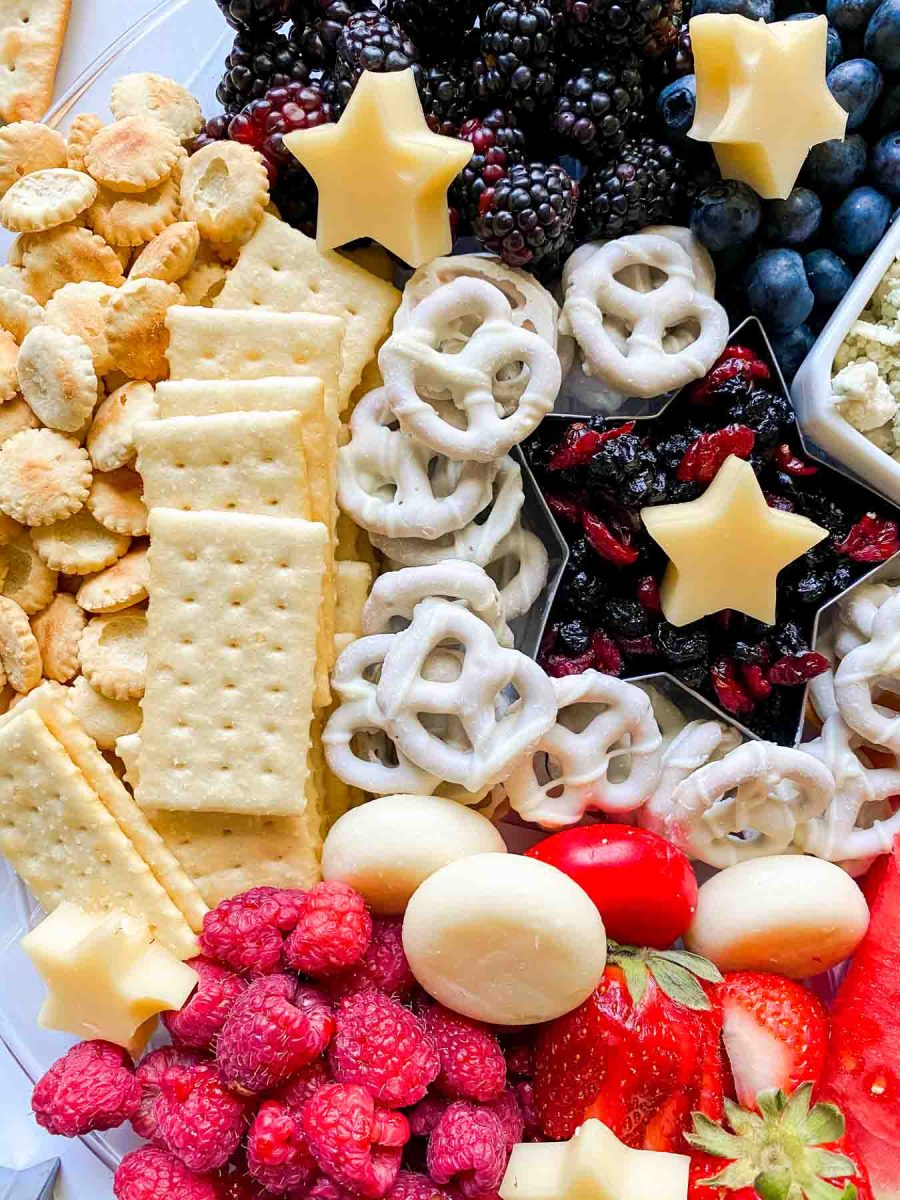 Charcuterie board for summer featuring fresh fruits, cheeses, crackers, dried fruits and candy coated pretzels. Hostess At Heart
