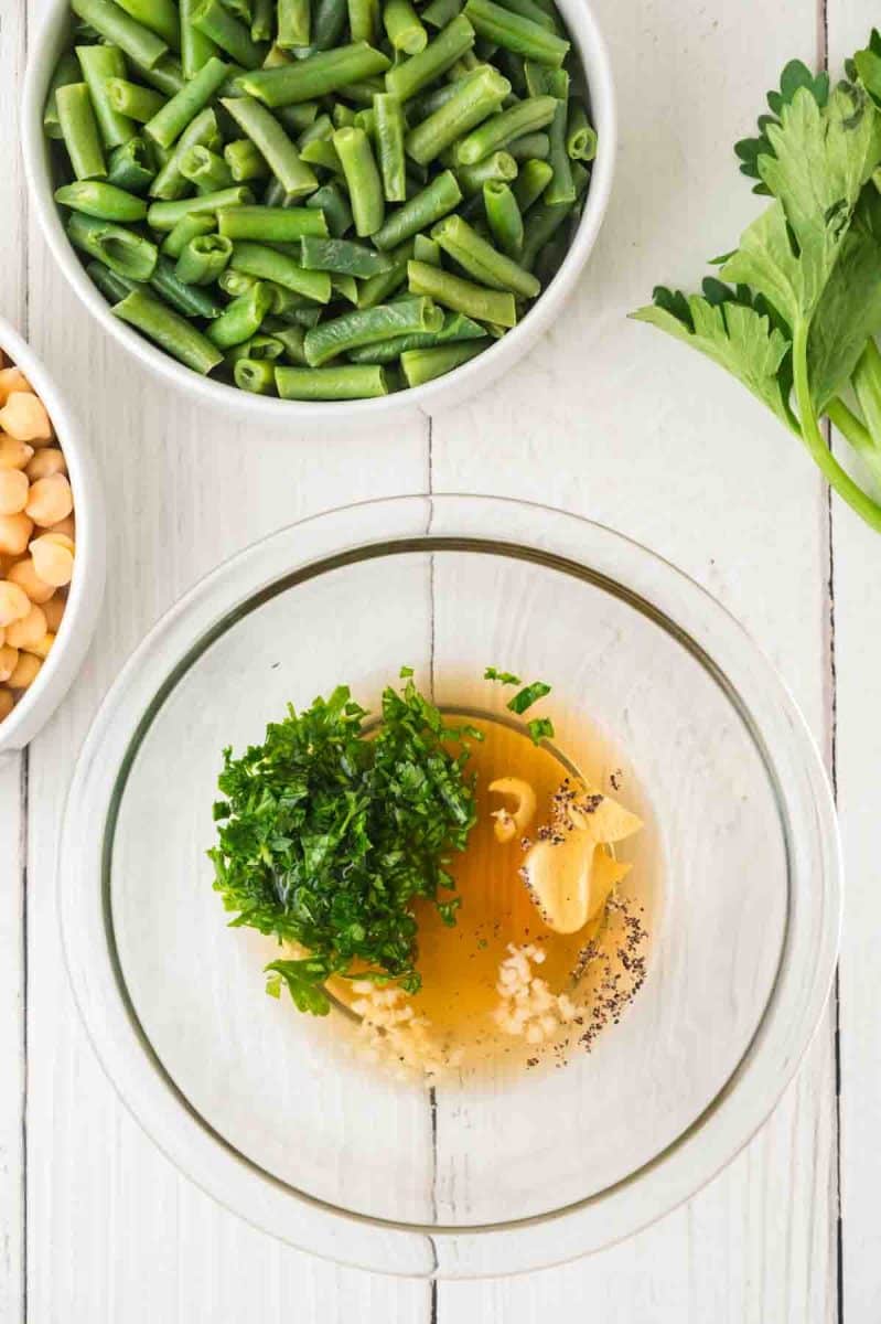 Apple cider vinegar, maple syrup, parsley, garlic, salt, and pepper in a bowl to make a dressing for three bean salad. Hostess At Heart