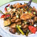Angled view of a Mongolian chicken stirfry loaded with crispy chicken and beautifully cooked vegetables over a serving of rice on a plate. Hostess At Heart