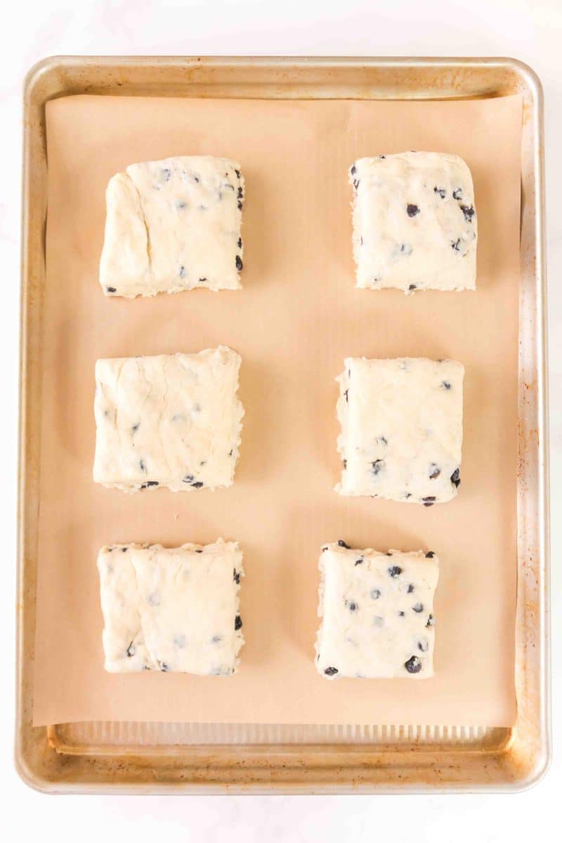 Six large blueberry biscuits on parchment-lined baking sheet before baking. Hostess At Heart