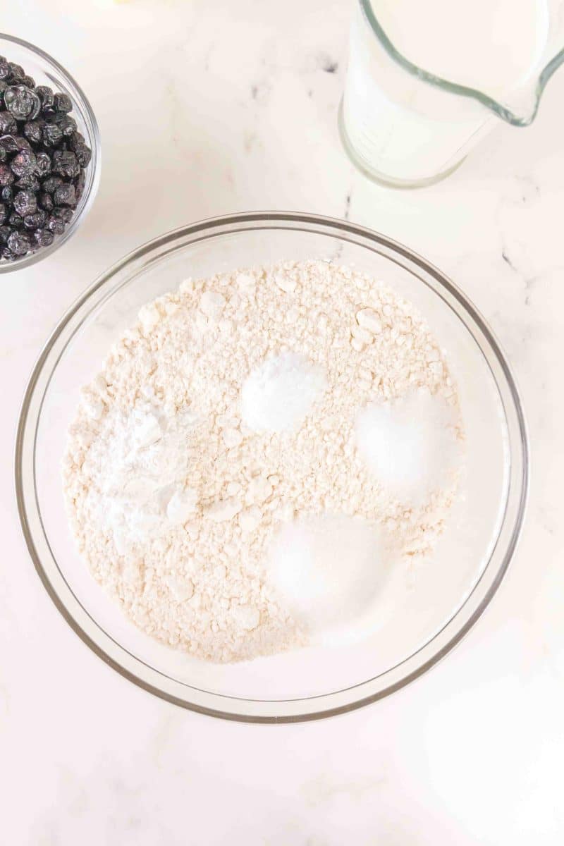 A mixing bowl filled with dry ingredients to make blueberry biscuits from scratch: flour, baking soda, salt, and sugar. Hostess At Heart