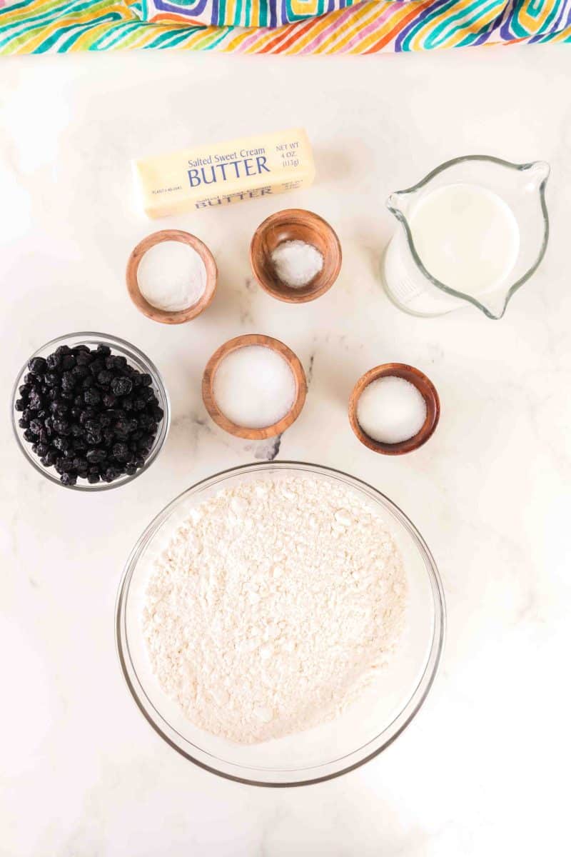 Ingredients for homemade blueberry biscuit recipe: flour, sugar, milk, butter, baking soda, powdered sugar, dried blueberries, and salt. Hostess At Heart