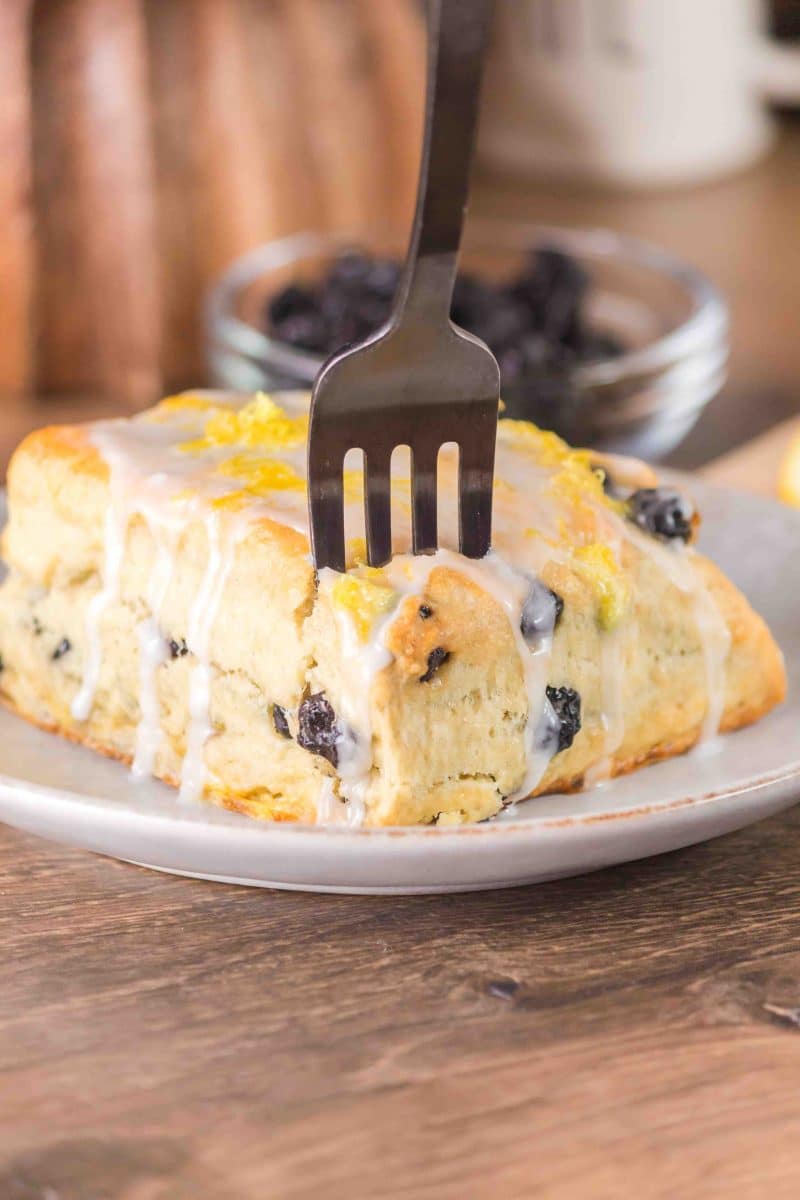 Freshly baked Blueberry biscuit with a fork inserted ready for a bite on a plate. Hostess At Heart