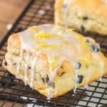 Angled view of a golden brown blueberry breakfast biscuit on a cooling rack with dripping vanilla glaze. Hostess At Heart