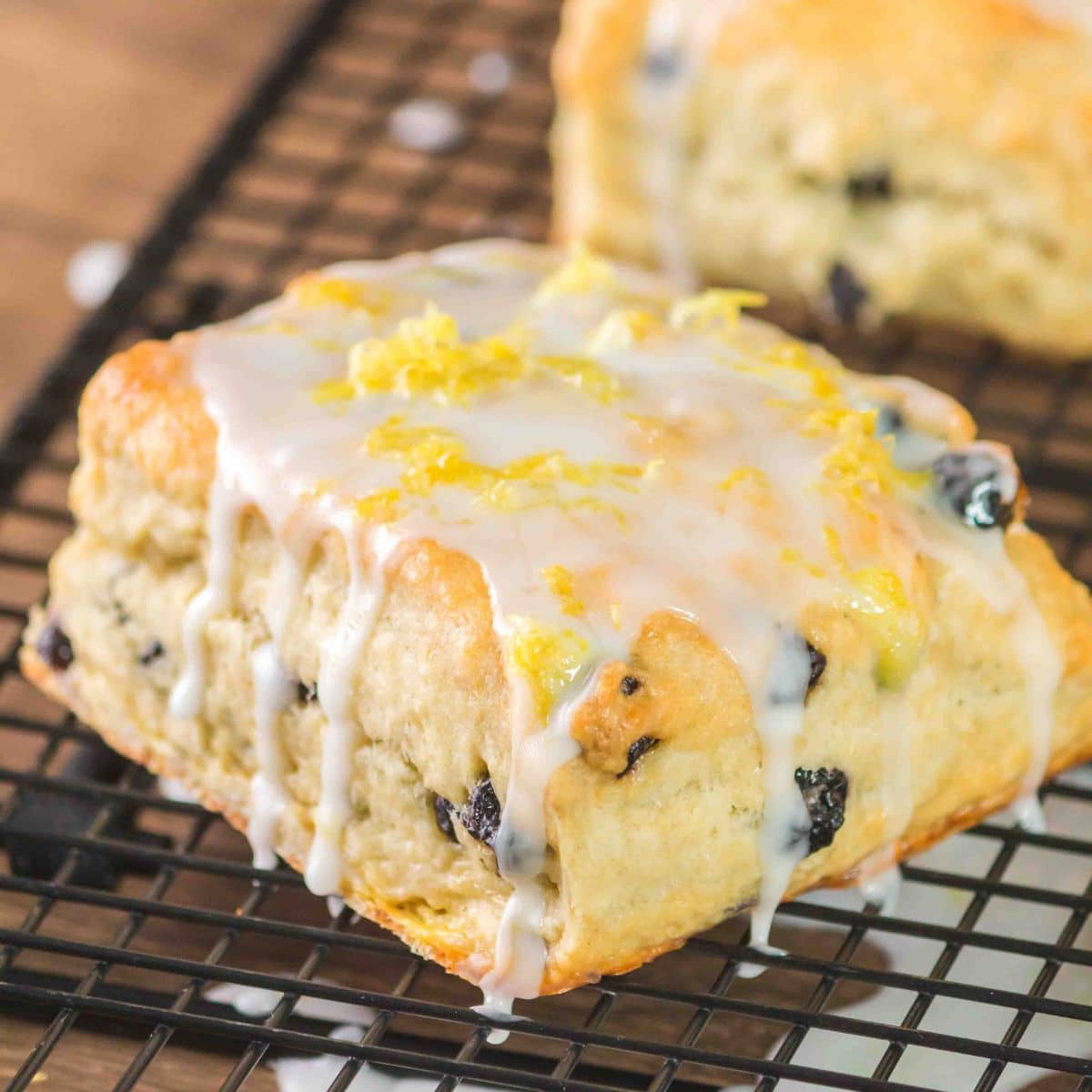 Angled view of a golden brown blueberry breakfast biscuit on a cooling rack with dripping vanilla glaze. Hostess At Heart