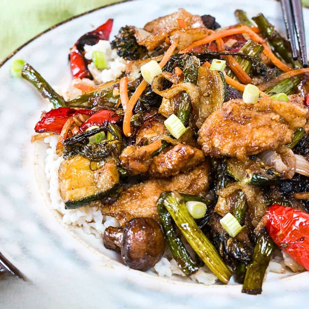 Angled view of a serving plate filled with rice and topped with colorful stirfried asperagus, red pepper, mushrooms, and zucchini. Hostess At Heart