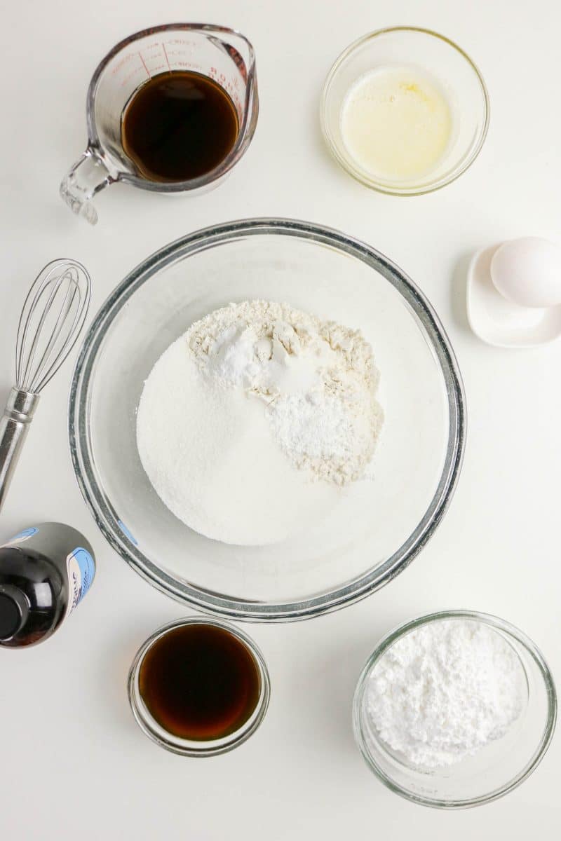 Mixing bowl filled with coffee donuts dry ingredients surrounded by the remaining ingredients to be added to make coffee doughtnut batter. Hostess At Heart
