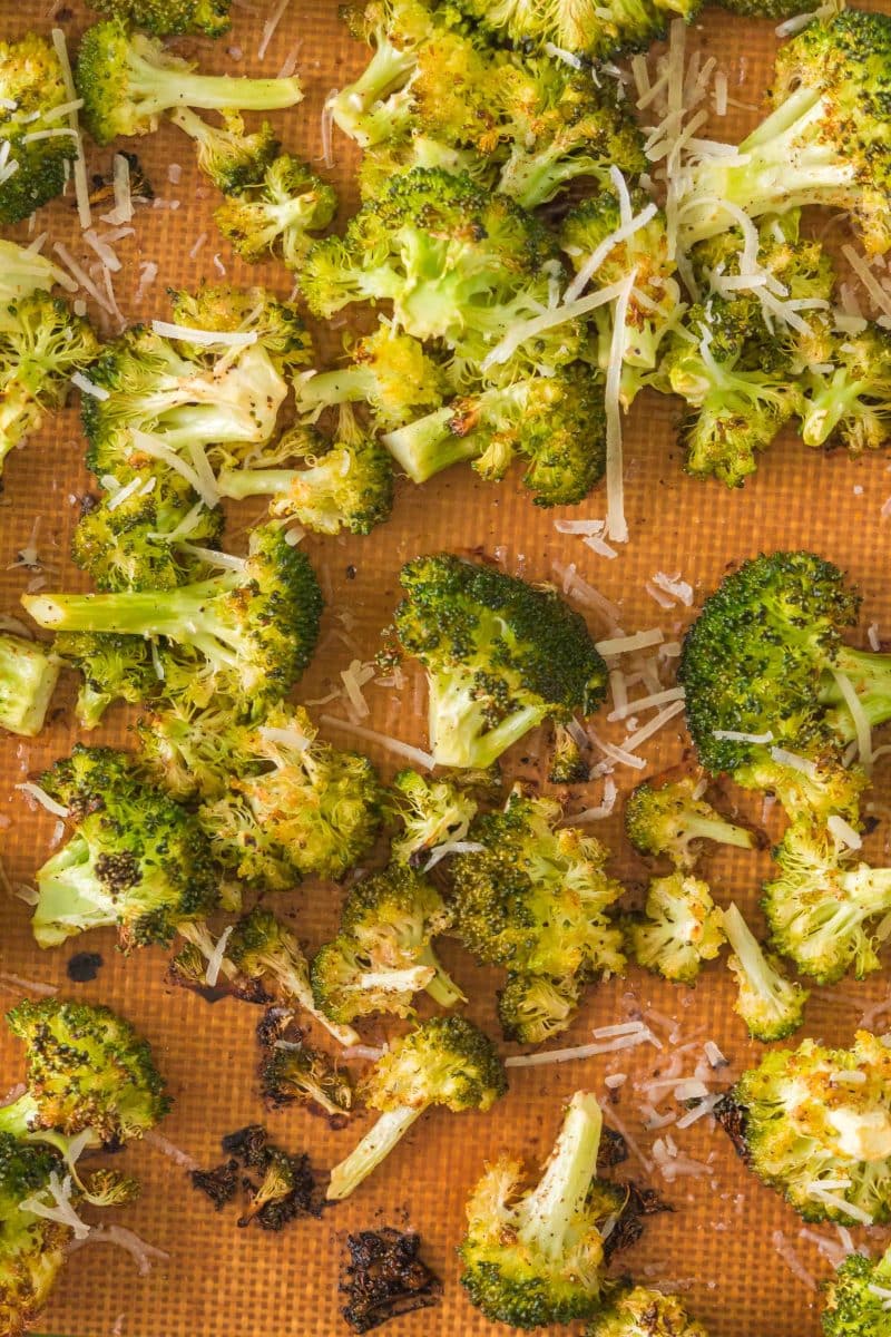 Crispy oven roasted broccoli topped with fresh Parmigiano on a baking sheet. Hostess At Heart
