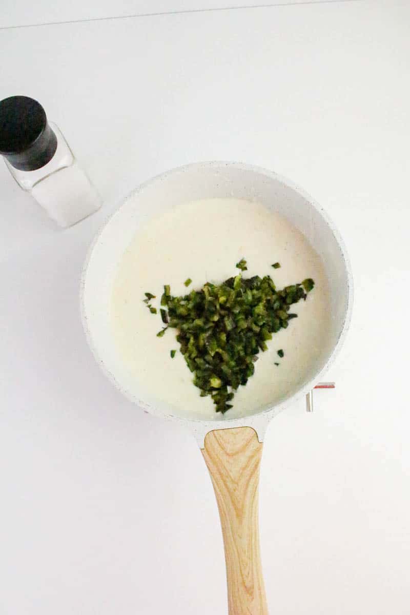 Finely chopped roasted poblano peppers added to a saucepan filled with creamy white queso cheese sauce. Hostess At Heart