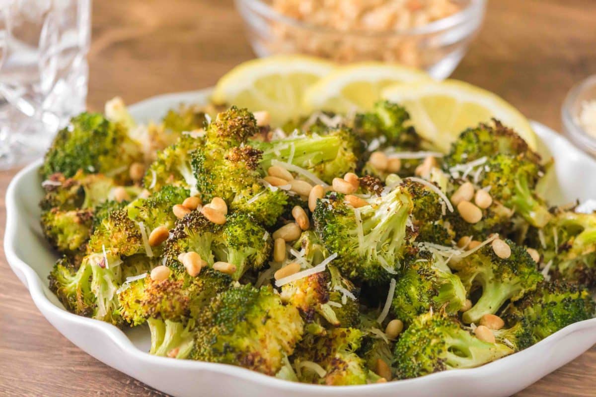 Sideview of oven roasted broccoli recipe with lemon, parmesan, and toasted pine nuts in a large serving bowl. Hostess At Heart