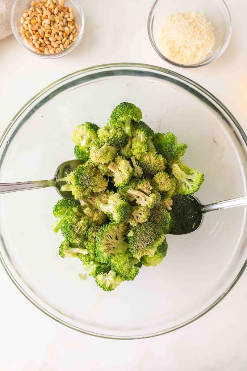 Broccoli florets in a large bowl being tossed with olive oil and lemon juice. Hostess At Heart