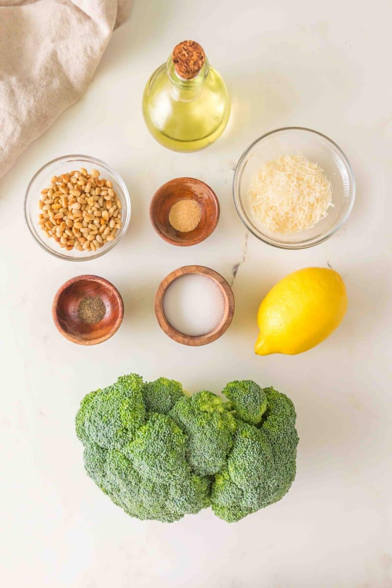 Ingredients for an easy crispy roasted broccoli recipe including a crown of broccoli, lemon, olive oil, pine nuts, salt, pepper, grated parmesan, and garlic powder. Hostess At Heart