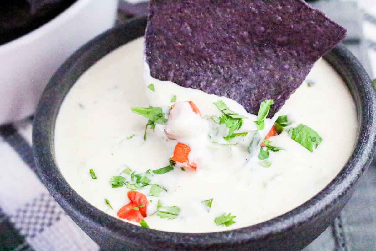 Tortilla chip dipping into warm smoky poblano queso cheese dip in a serving bowl. Hostess At Heart