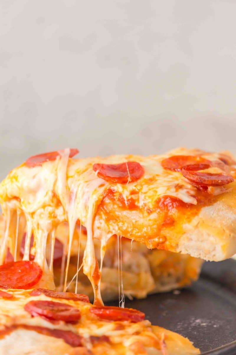 A slice of pepperoni pizza made with no knea dough being pulled from the pie showing a gooey cheese pull. Hostess At Heart