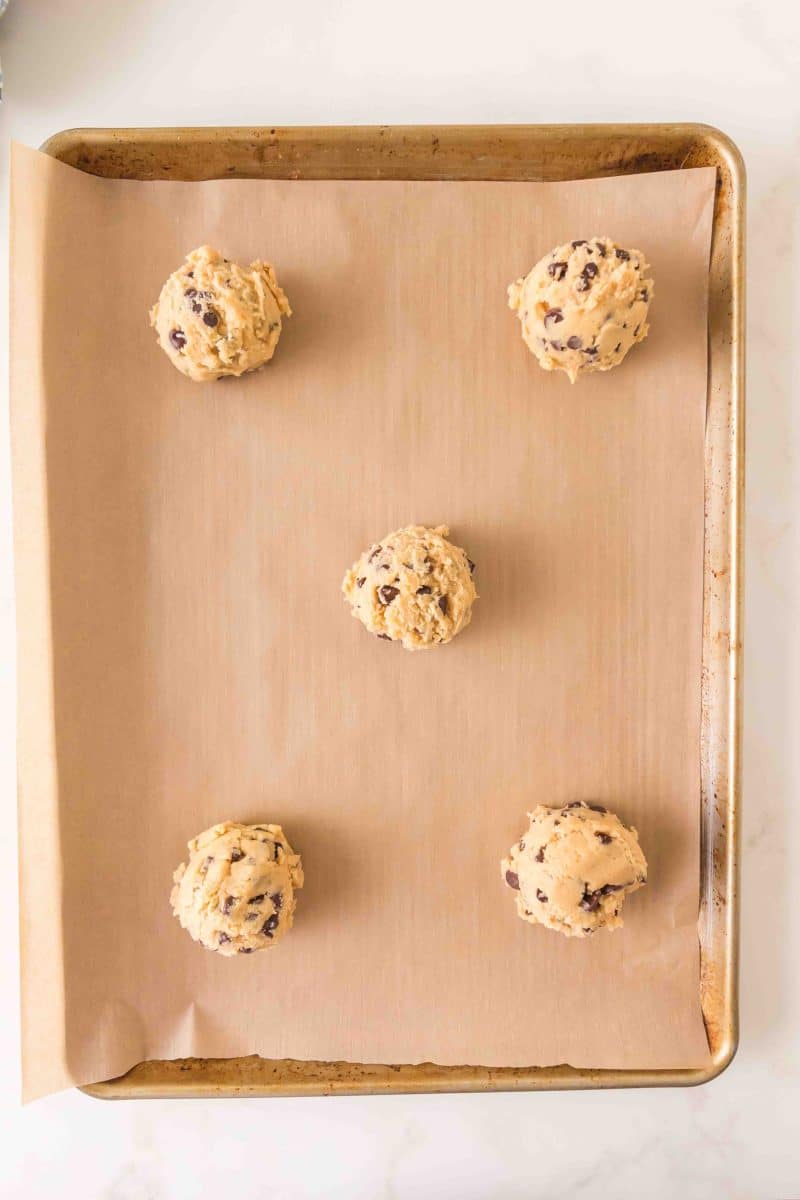 Scoops of crumbl cookie dough on parchment paper lined baking sheet. Hostess At Heart