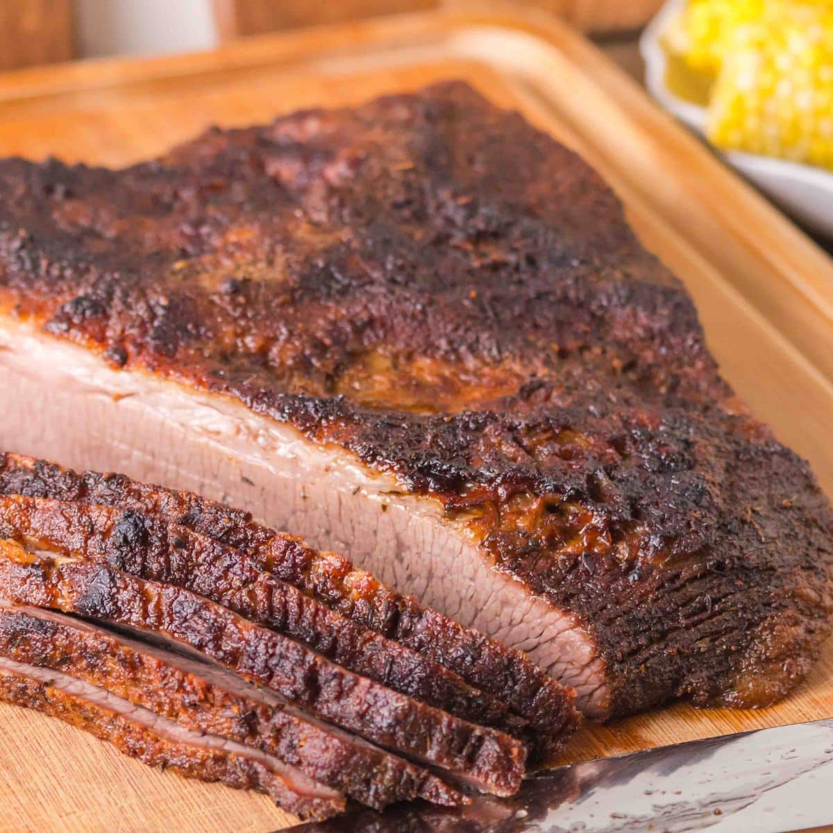 Sideview of a oven baked brisket with a juicy crust with 5 slices laying in front of it on a cutting board. Hostess At Heart