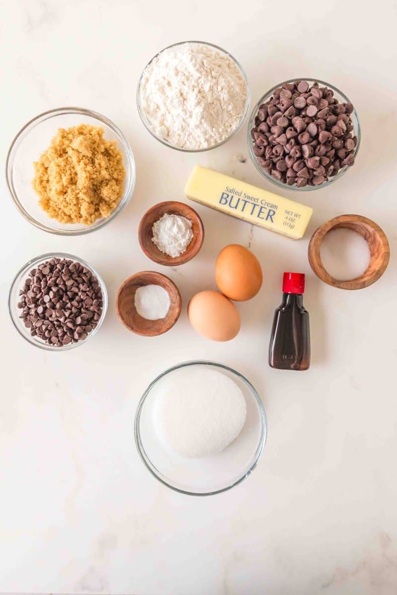 Ingredients to make a crumbl chocolate chip cookie recipe including, flour, baking soda and powder, sugar, white and brown, vanilla, salt, eggs, chocolate chips, and butter. Hostess At Heart