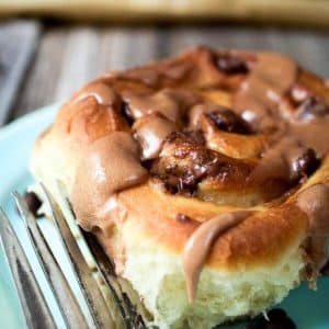 A plate holding a sweet yeast roll filled with chocolate chips and topped with a sweet chocolate brownsugar malt glaze. Hostess At Heart