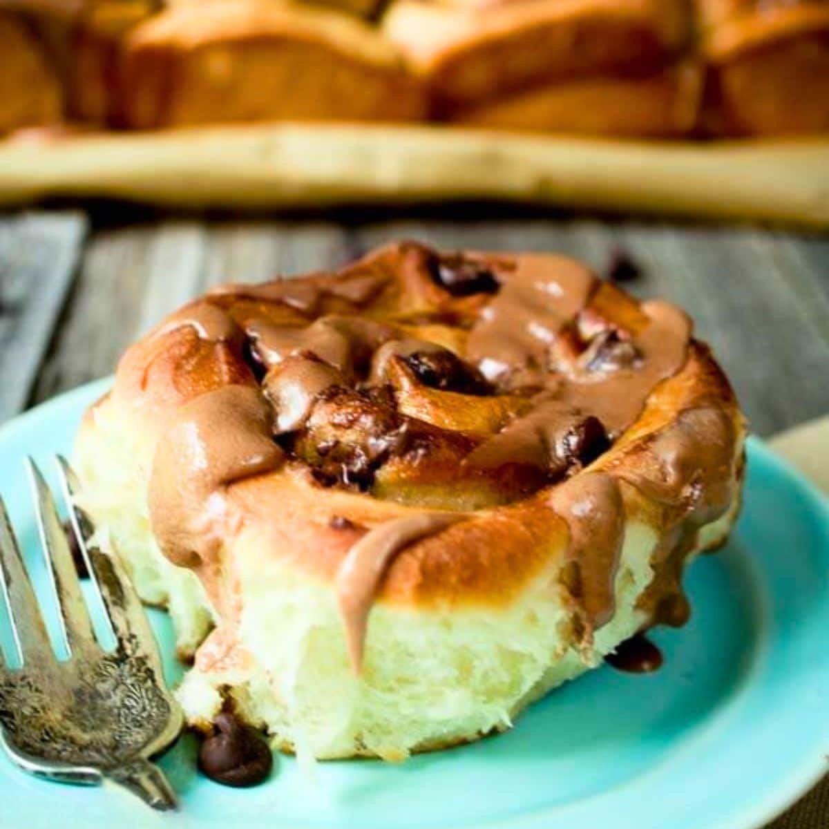 A sideview of a soft and tender cinnamon brown sugar roll stuffed with chocolate chips and glazed with a malt flavored brown sugar glaze. Hostess At Heart