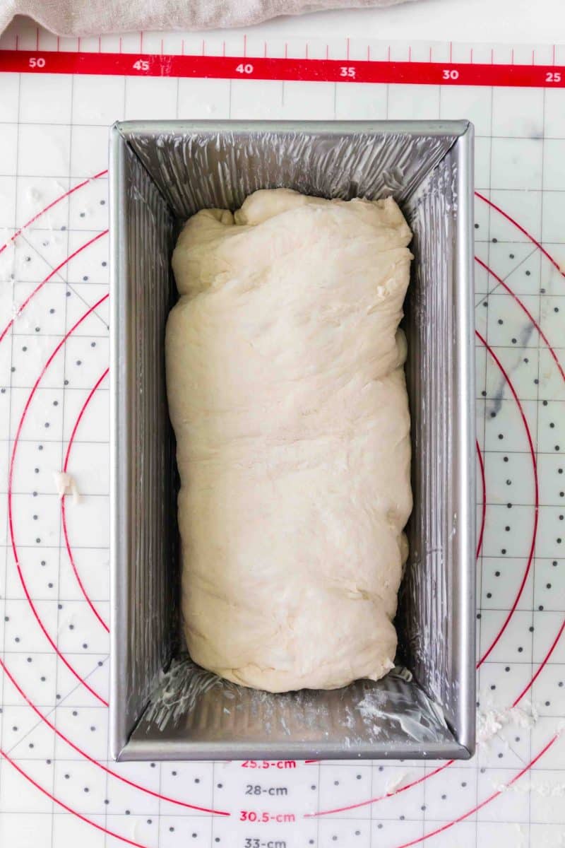 A shaped loaf of bread dough in a greased loaf pan for rising. Hostess At Heart