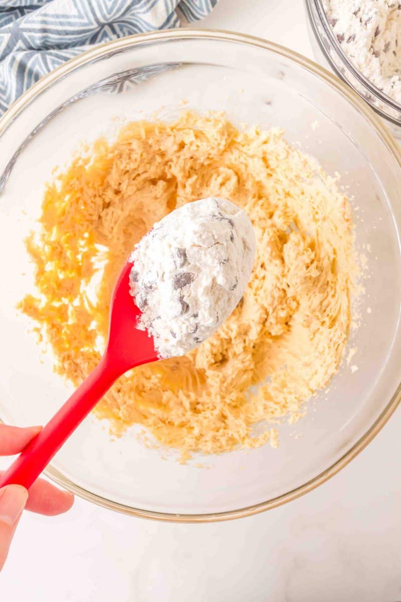 A spoon holding a dry crumble cookie ingredients mixed with chocolate chips into creamy batter to bake up crumble chocolate chip cookies recipe. Hostess At Heart