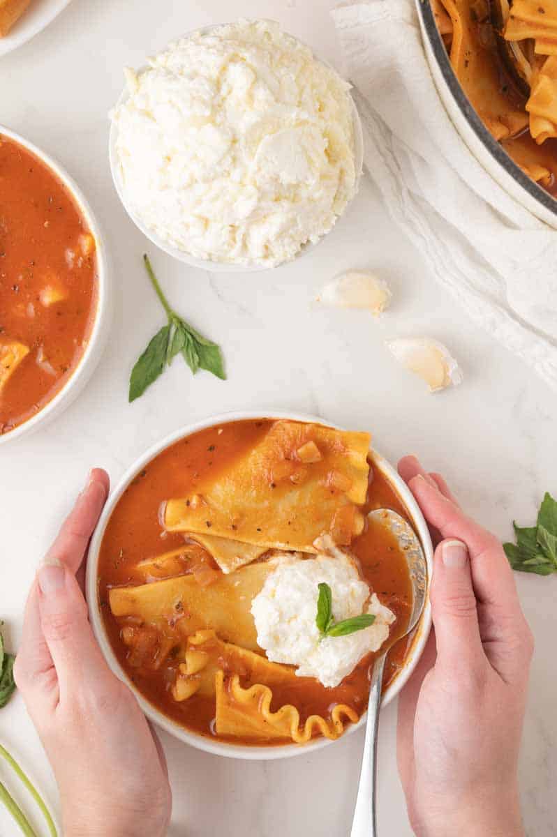 Overhead view of a bowl of one-pot lasagna soup filled with a rich tomato broth, broken lasagne noodles, and a dollop of a cheesy ricotta mixture. Hostess At Heart