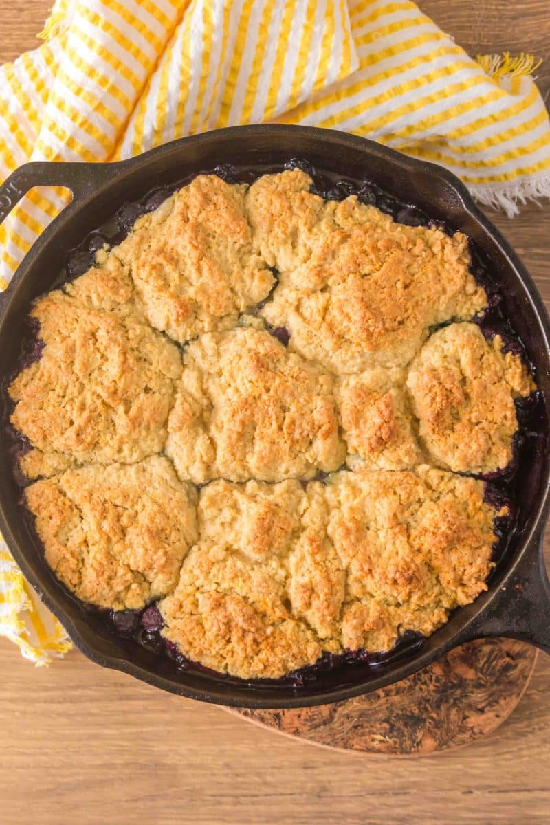 Top down closeup of golden sourdough discard blueberry cobbler fresh from the oven in a cast iron skillet with blueberry filling around the edges. Hostess At Heart