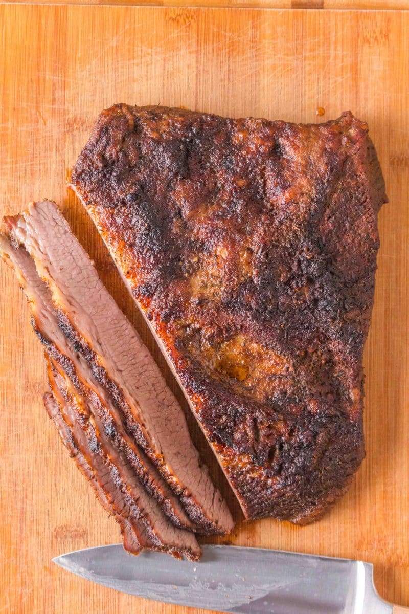 Top view of an oven baked brisket with a juicy brown bark sitting on a cutting board with 5 slices fanned out in front of it ready for serving. Hostess At Heart